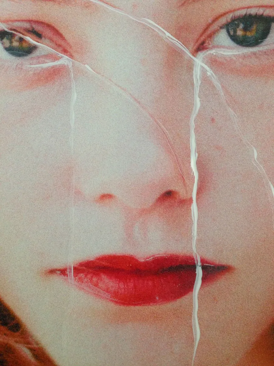 Close-up of a woman’s face with red lips, white lines trailing from her eyes like tears